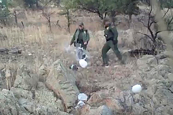 Agentes de la Patrulla Fronteriza patean contenedores plsticos de agua.